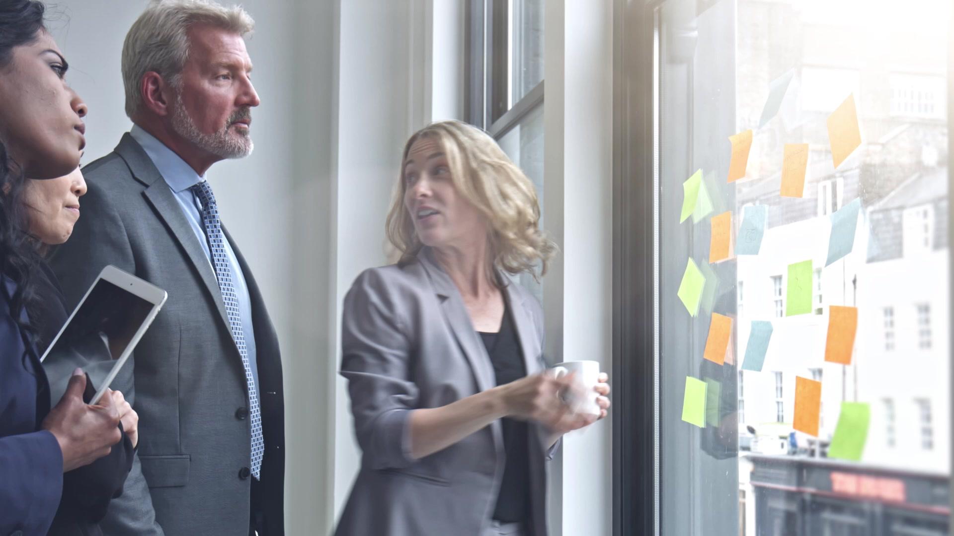 Two colleagues reviewing ideas on a glass wall covered in sticky notes